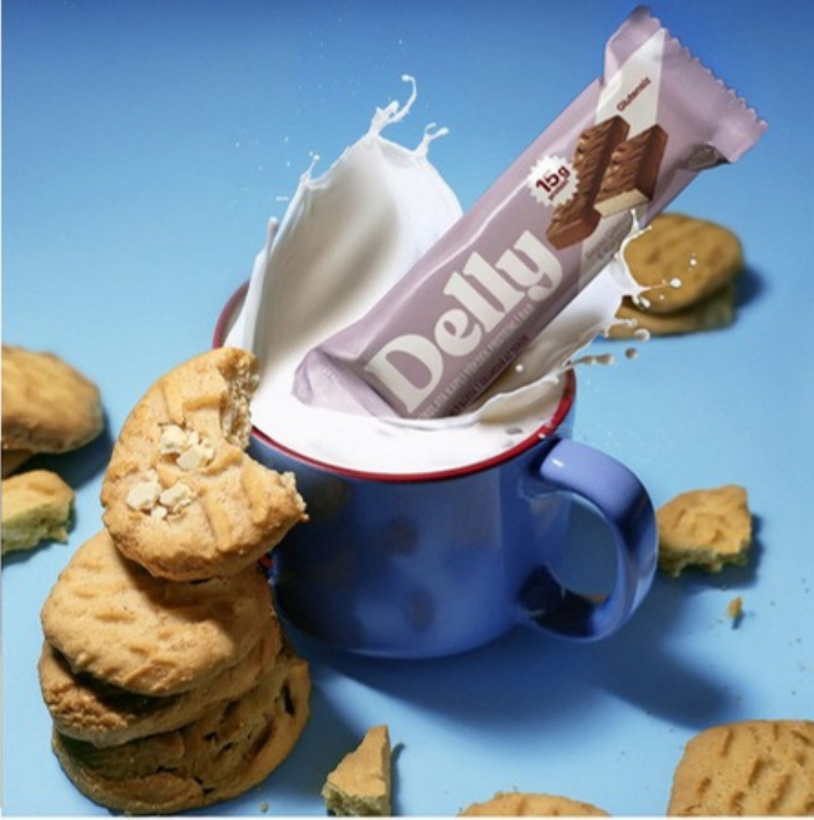 Delly bar splashing into a blue mug of milk beside biscuits